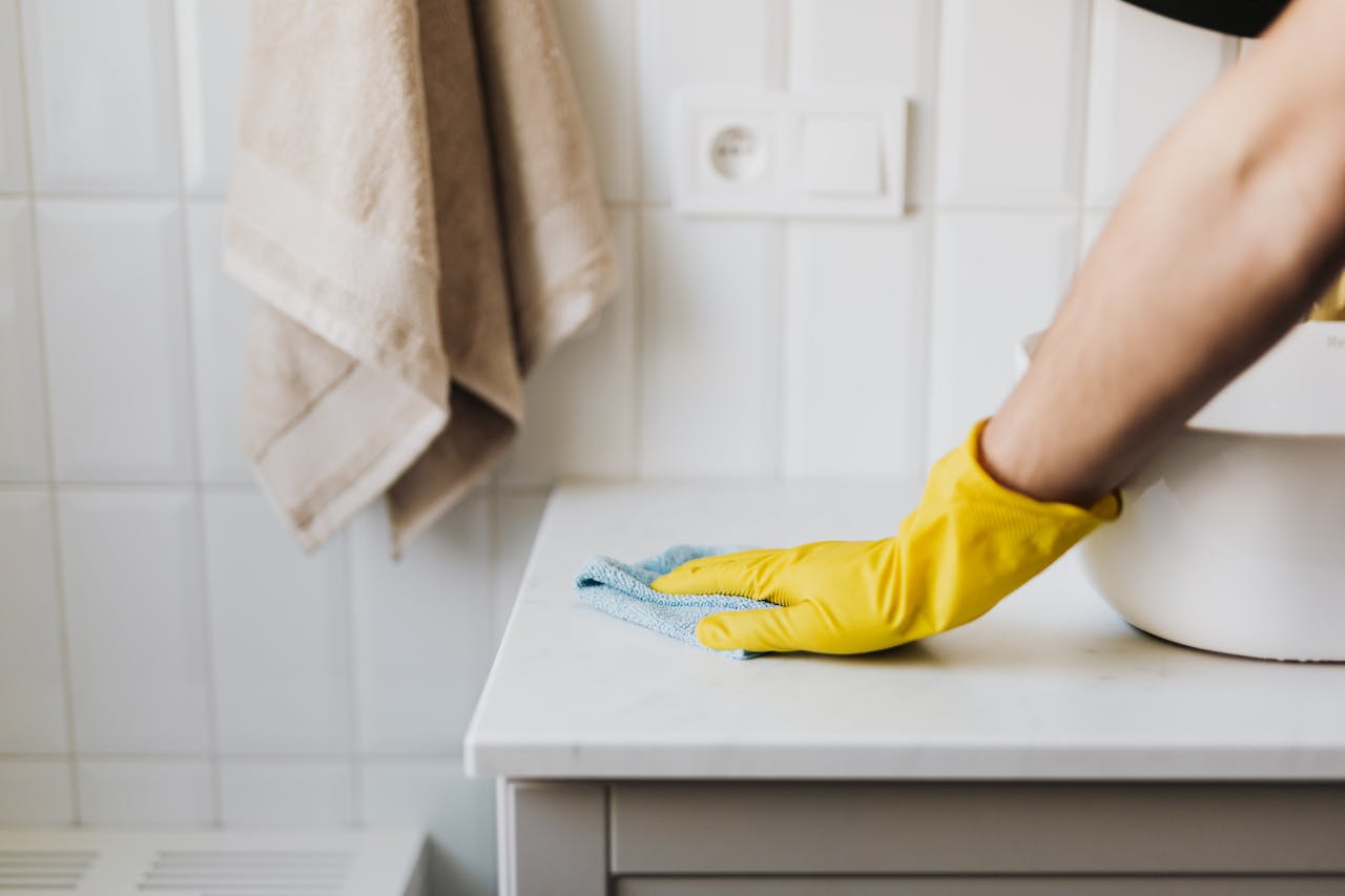 Crafting Captivating Headlines: Your awesome post title goes here Close-up of a person wearing yellow gloves wiping a bathroom counter with a cloth.
